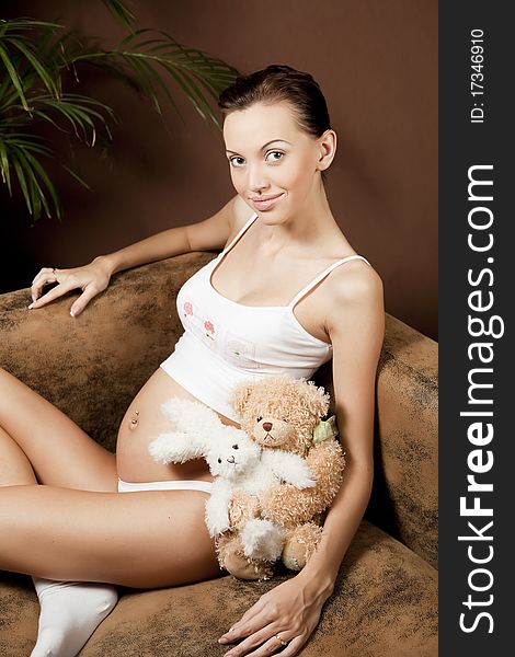 Pregnant woman, sitting on the sofa with toys and smiling