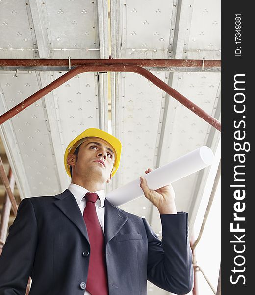 Mid adult caucasian architect holding blueprints in construction site. Vertical shape, low angle view, waist up. Mid adult caucasian architect holding blueprints in construction site. Vertical shape, low angle view, waist up
