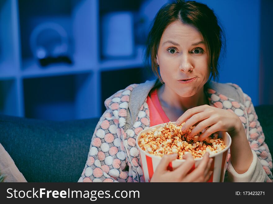 Young lady is watching TV laughing and eating popcorn having fun at home alone enjoying modern television. Youth lifestyle and cheerful people concept.