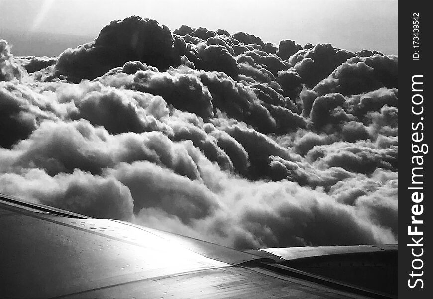under the wing of an airplane sky with clouds black and white flying high like a bird
