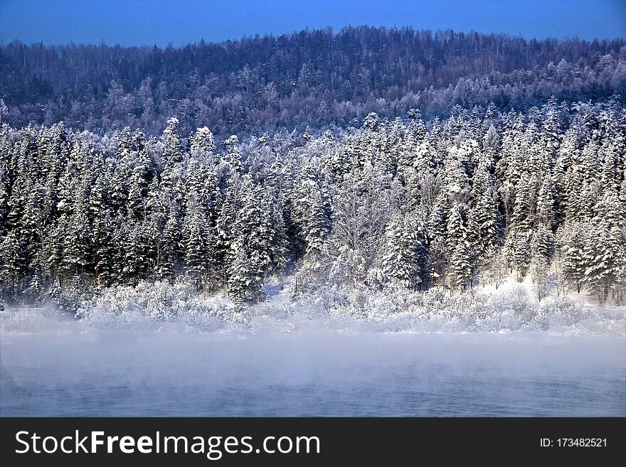 Winter landscape. In the background conifer winter forest. In the foreground - mist rising from the water