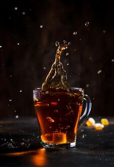 Splash In Glass Cup Of Black Tea With Natural Steam On Brown Background Stock Images