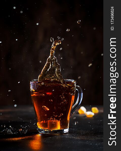 Splash in glass cup of black tea with natural steam on brown background