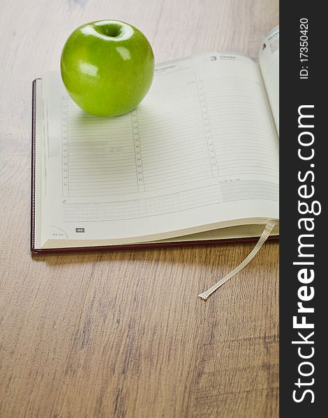 Notebook with apple on wooden background