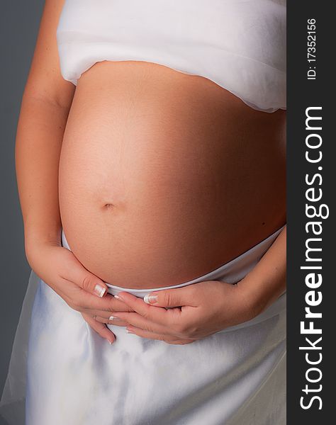 Pregnant woman staing on grey background, close up. Pregnant woman staing on grey background, close up