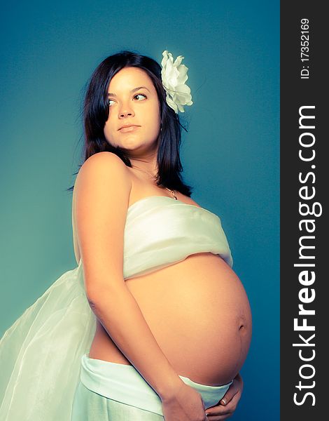 Beautiful pregnant woman staing on grey background. Toned as cross-procesed photos