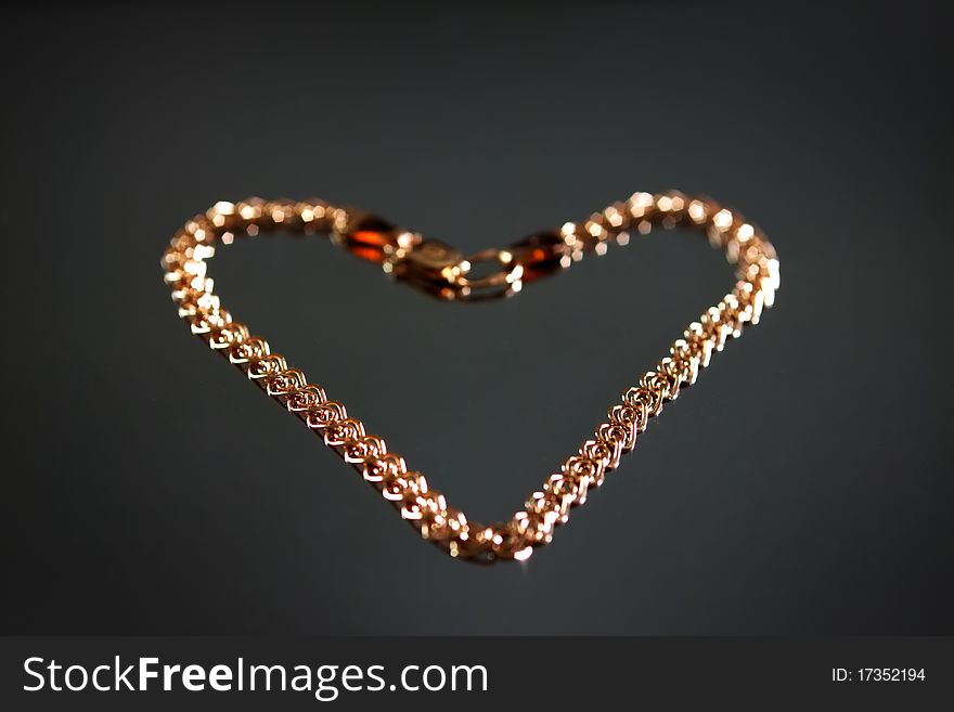 Gold bracelet in the shape of a heart on a gray background