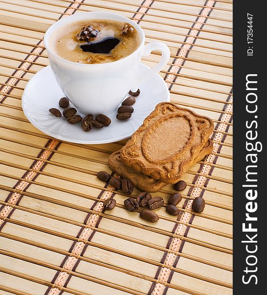 Cup of capuchino with coffee beans and cookie on a mat