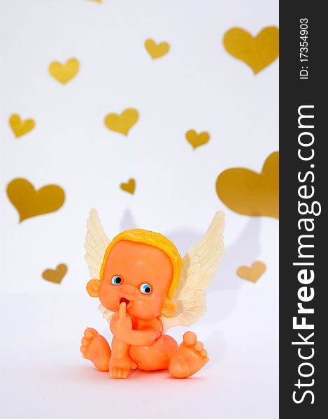 Funny shy toy angel puts his finger in mouth on white background with golden hearts. Funny shy toy angel puts his finger in mouth on white background with golden hearts