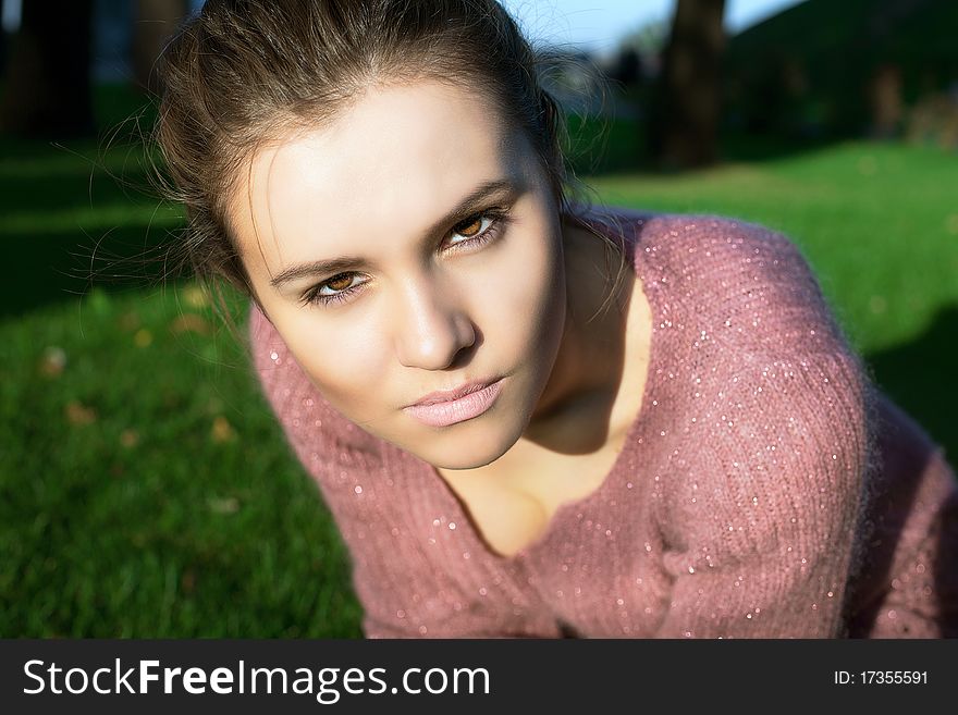 A beautiful young brunette in pink clothes sits on a green lawn. A beautiful young brunette in pink clothes sits on a green lawn