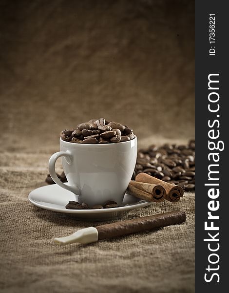 Cup with coffee beans and cinnamon on burlap background