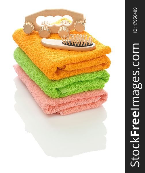 Stack of pink green and orange towels with massager and wooden hairbrah isolated on white background. Stack of pink green and orange towels with massager and wooden hairbrah isolated on white background