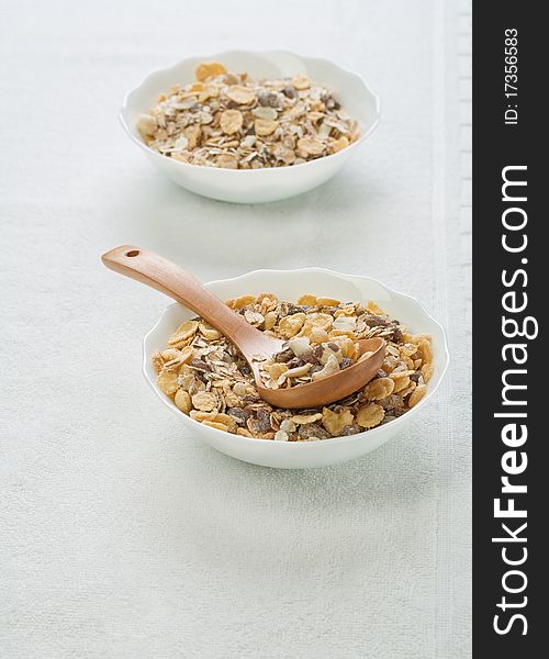 Muesli in bowls with one wooden spoon on white background of white cotton towel