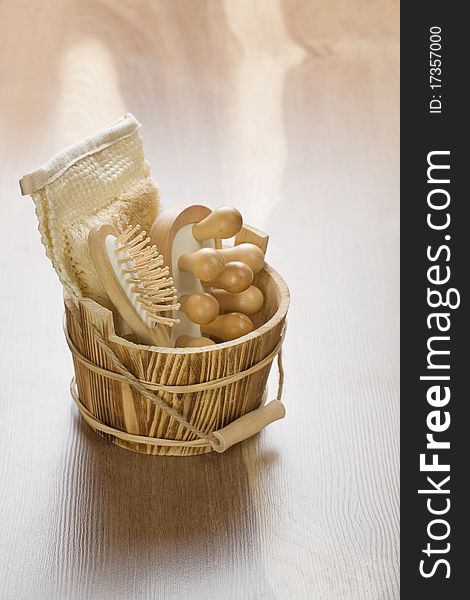 Brown wooden bucket with wooden massager hairbrush and bast on wooden background. Brown wooden bucket with wooden massager hairbrush and bast on wooden background