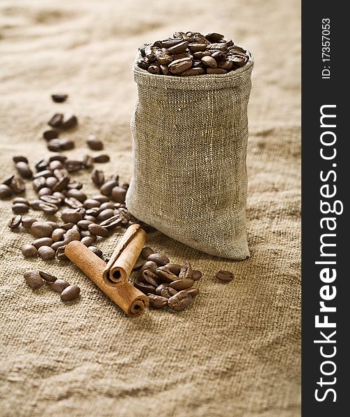 Coffee grains in burlaps bag with stick of cinnamon on the background of sacking. Coffee grains in burlaps bag with stick of cinnamon on the background of sacking