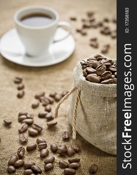 Coffee beans in bag and on the background and cup of coffee. Coffee beans in bag and on the background and cup of coffee