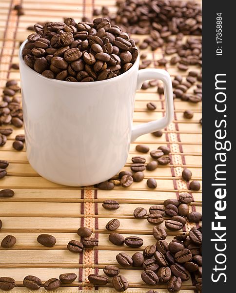 Composition white ceramic cup with coffee beans on wooden yellow mat. Composition white ceramic cup with coffee beans on wooden yellow mat