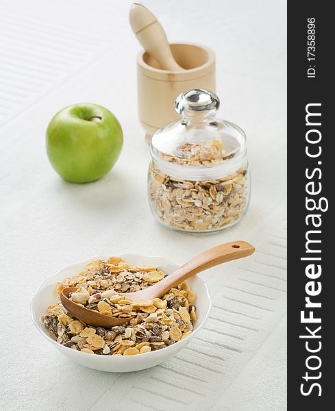 Composition of muesly in glass jar and white ceramic bowl and green apple and wooden mortar with pestle on white background. Composition of muesly in glass jar and white ceramic bowl and green apple and wooden mortar with pestle on white background