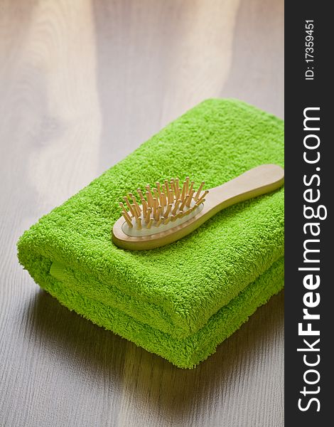Green cotton towel and wooden hairbrush on wooden background
