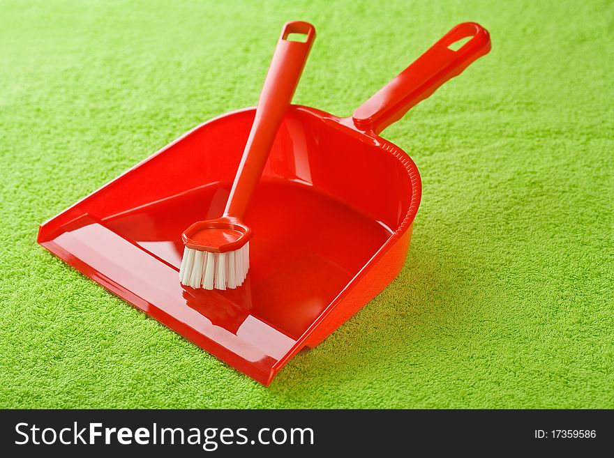 Red dustpan with brush on green cotton towel