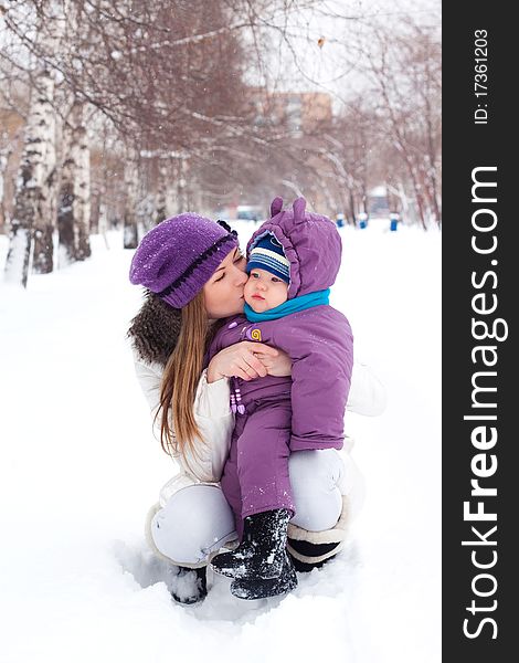 Mother kissing and holding a baby, snow, winter park, walk. Mother kissing and holding a baby, snow, winter park, walk