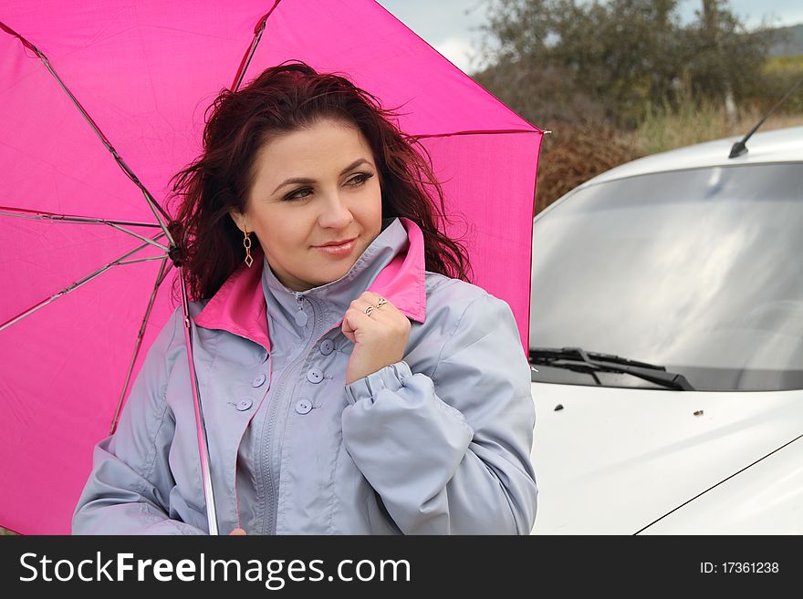 Beautiful lady with bright pink umbrella standing near her car. Beautiful lady with bright pink umbrella standing near her car