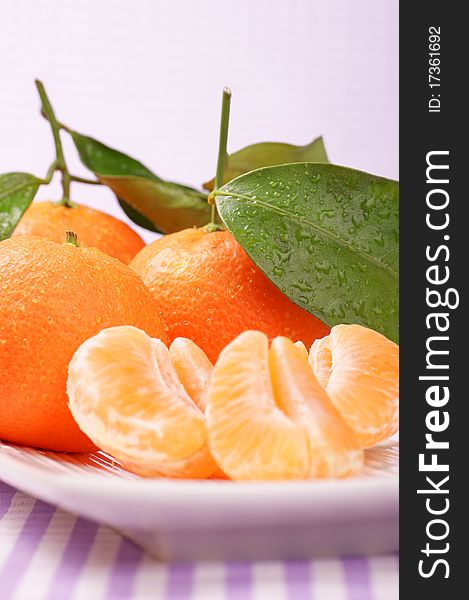 Whole and sectioned clementines served on a white dish. Studio shot. Selective focus, extra-shallow DOF.