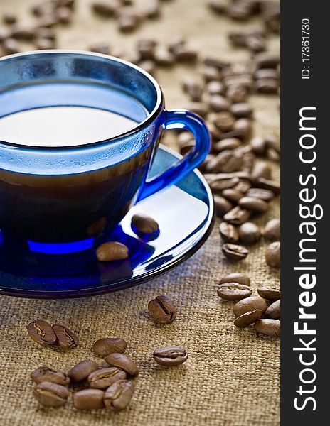 Coffee beans with blue glass cup on saucer and on the background of sacking. Coffee beans with blue glass cup on saucer and on the background of sacking