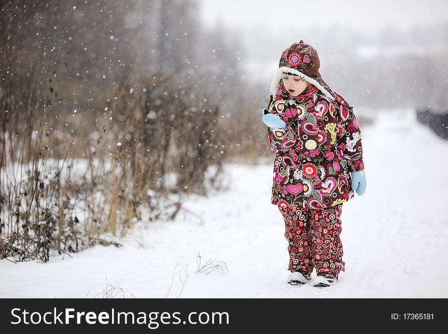 Adorable small girl in colorful winter clothers catches snowflakes in strong snowfall. Adorable small girl in colorful winter clothers catches snowflakes in strong snowfall