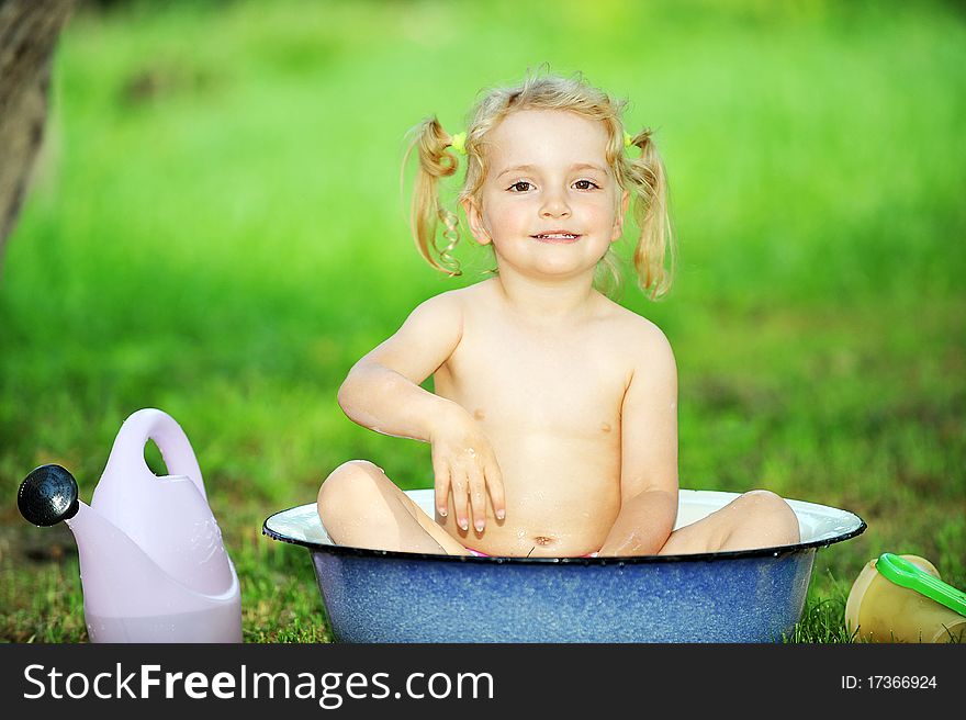 Little girl sits in basin with water. Hot summer day