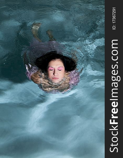 A woman in a dress in the water coming out of it with her eyes closed. A woman in a dress in the water coming out of it with her eyes closed.