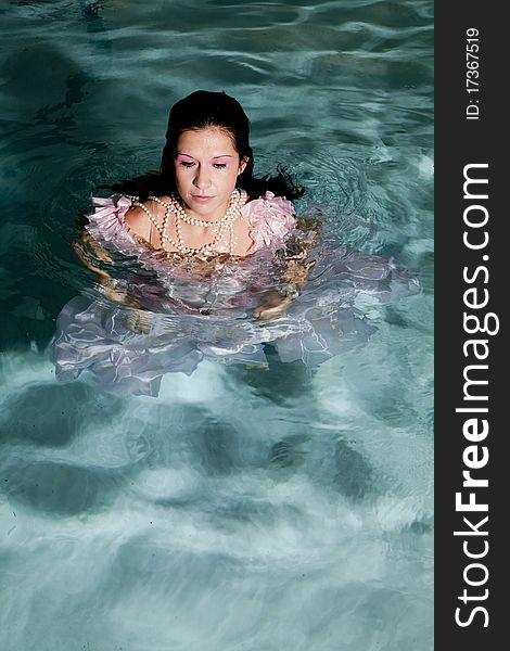 A woman standing in water in her fancy pink dress with her pearl necklace on with a peaceful expression on her face. A woman standing in water in her fancy pink dress with her pearl necklace on with a peaceful expression on her face.