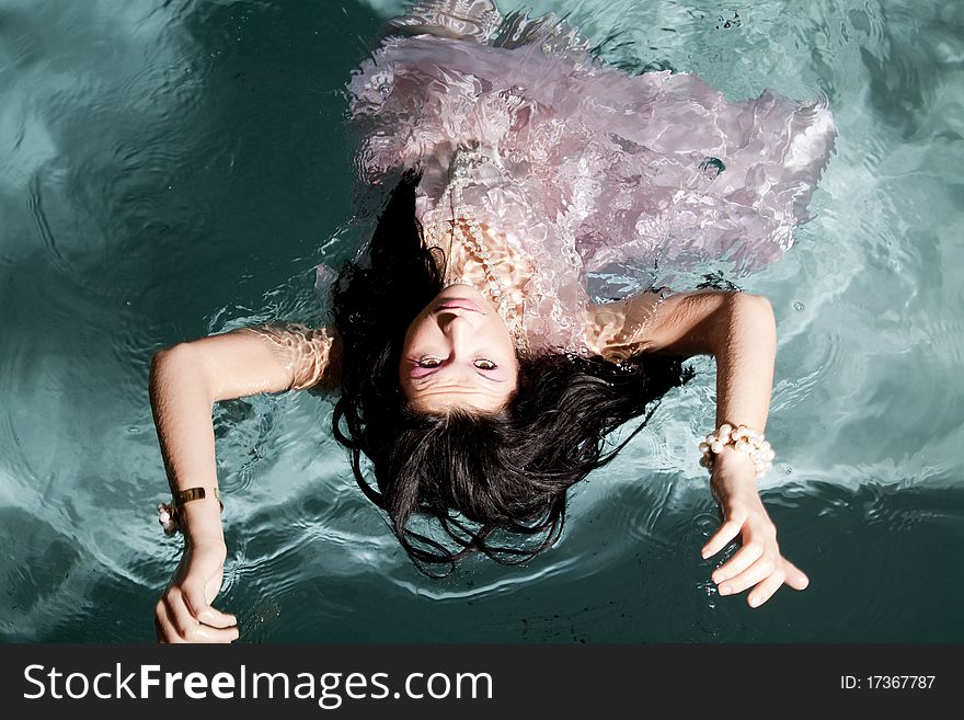 A woman laying on her back looking at the camera while she floats in the water in her pink dress. A woman laying on her back looking at the camera while she floats in the water in her pink dress.