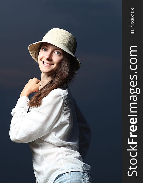 Portrait of a young smiling beautiful woman standing in darkness in a hat