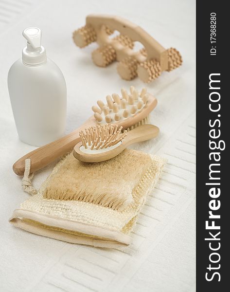 Bathing accessories brown wooden massager. hairbrush. brush combination with massager white plastic spray bottle with liquid soap natural bast all its on the background of the white cotton towel