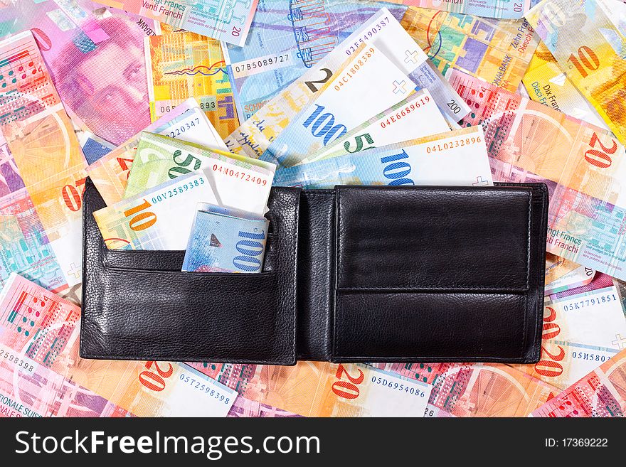 A black Wallet with Swiss Francs, is lying on a Table full of Swiss Francs. A black Wallet with Swiss Francs, is lying on a Table full of Swiss Francs