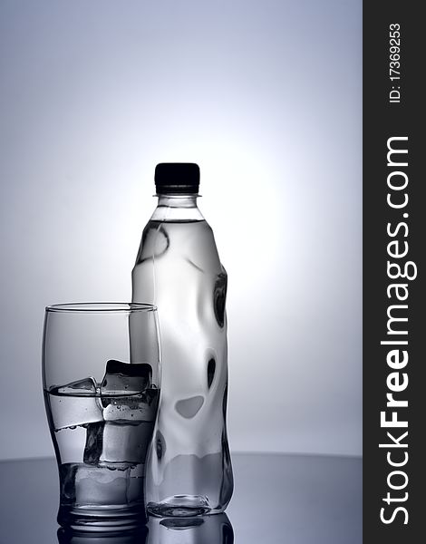 Glass of cold mineral water with ice and plastic bottle