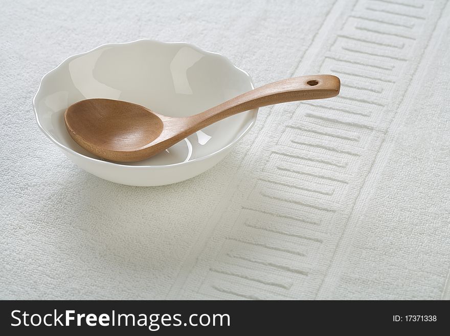 Studio shot wooden spoon in empty white ceramic bowl on white cotton fabric. Studio shot wooden spoon in empty white ceramic bowl on white cotton fabric