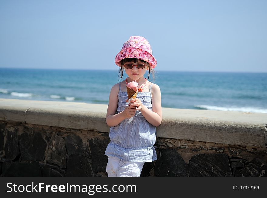 Small girl in glasses and sun hat on sea background with ice cream. Small girl in glasses and sun hat on sea background with ice cream