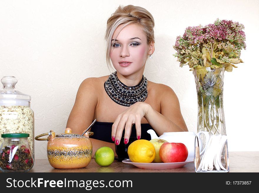 Woman with cup, jasmin petals, lemon, apple, tea and autumn flowers against yellow wall at home