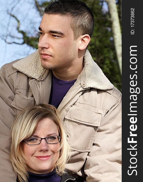 Autumn - outdoor shot of two young people as a close couple, satisfied looking. The man holds the woman standing behind her.