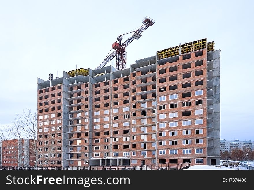 Tower crane near the house under construction on the background of a cloudy sky. Tower crane near the house under construction on the background of a cloudy sky