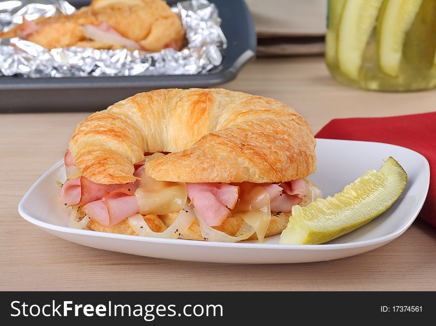 Ham and cheese sandwich on a croissant roll with a pickle