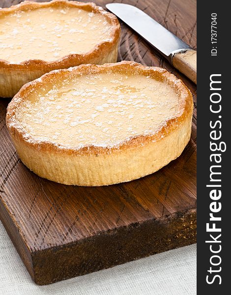 Two lemon tarts on a wooden serving board