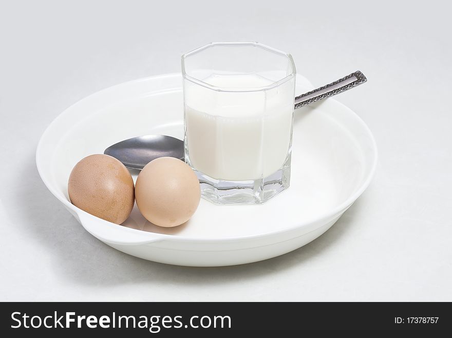 A glass of milk and two eggs in a white porcelain plate