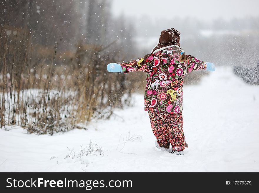 Adorable small girl in colorful winter clothes plays with snow in strong snowfall. Adorable small girl in colorful winter clothes plays with snow in strong snowfall