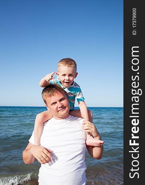 Father with son on shoulders on blue sky background on a beach. Father with son on shoulders on blue sky background on a beach