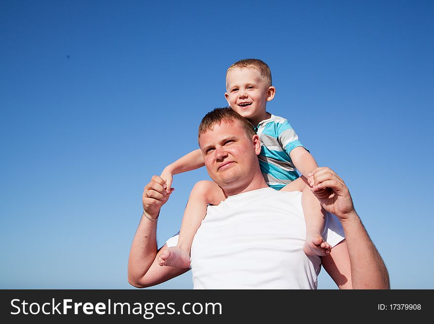 Father with son on shoulders on blue sky background on a beach. Father with son on shoulders on blue sky background on a beach