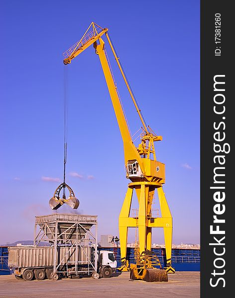 Yellow dock crane unloading material from a cargo ship