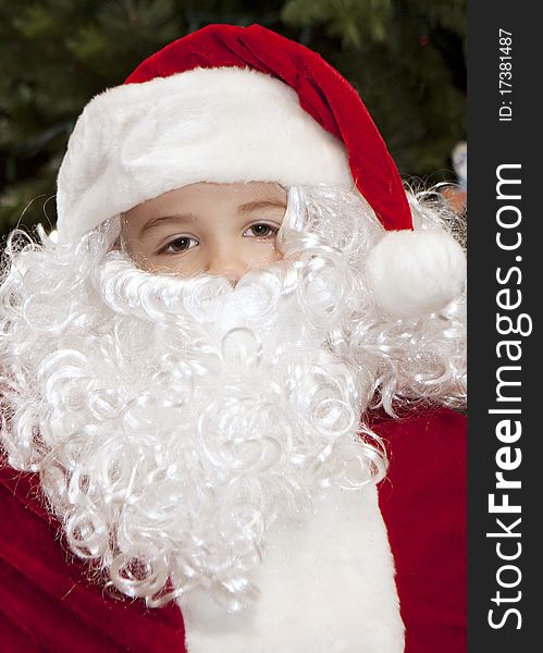 Thoughtful boy dressed as Santa Claus with a Christmas Tree backdrop.